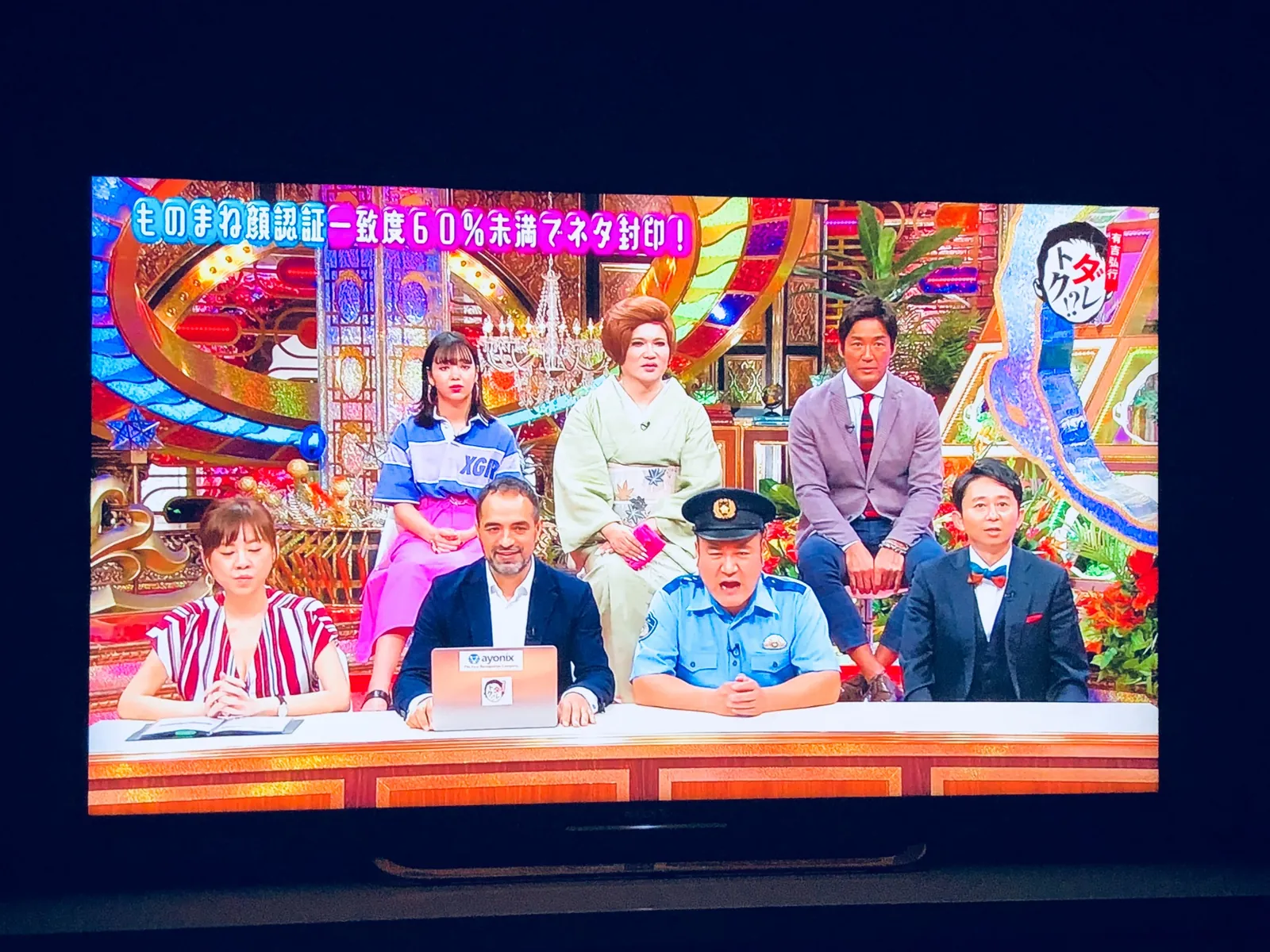 フジテレビ系『有吉弘行のダレトク!?』のスタジオを映したテレビの写真。出演者がデスクの後ろに並んでいます。