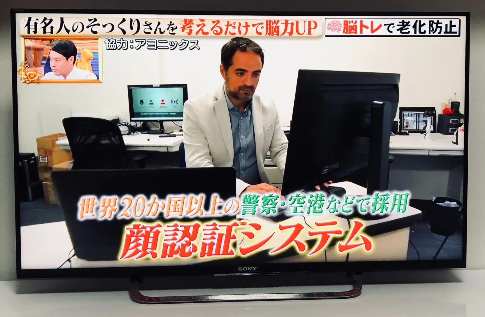 パソコンの前でAyonixの顔認証を実演するDr Sadi Vuralが映ったフジテレビの放送画面。