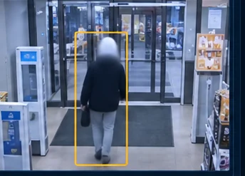 An exit-zone camera frame showing the same shopper walking toward the doors, inside a detection box